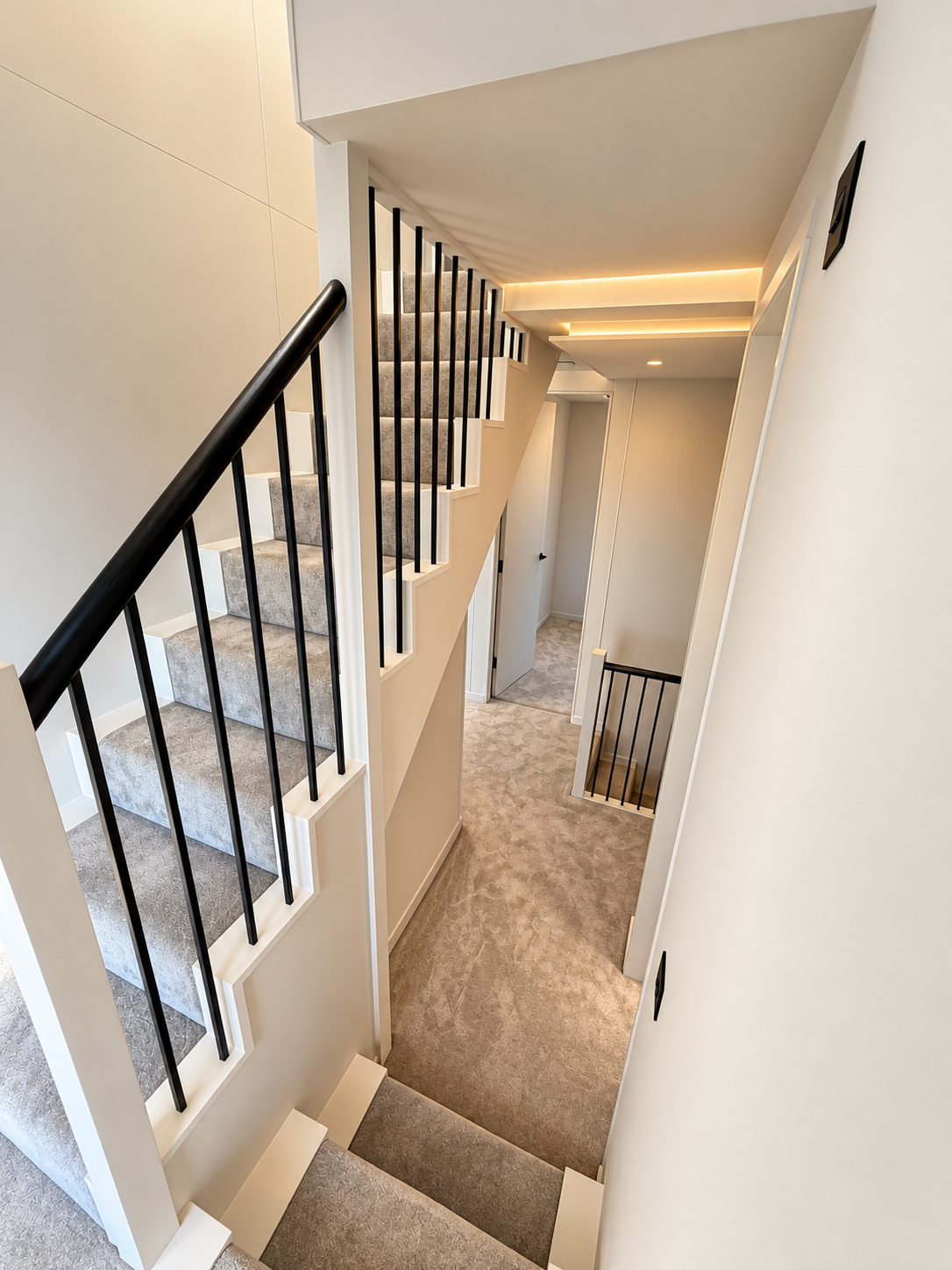 Upper landing with carpeted stairs, black balustrade and warm cove lighting